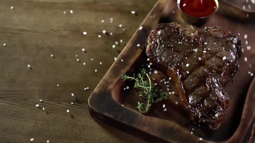 Thick barbecue salt is being added to grilled t bone steak on a steak board