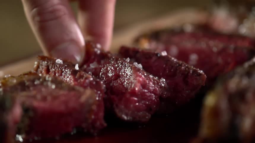 A mans hand takes up a slice of steak