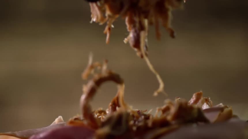 A person dropping meat on to a sandwich