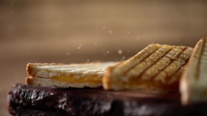Small cheese sandwiches topple over near the edge of a wooden platter