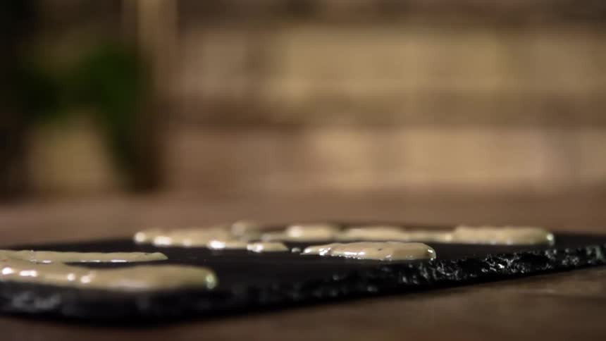 Hamburger bun falls over a black ceramic plate garnished with white sauce