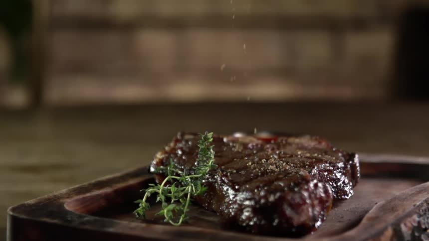 A slab of perfectly grilled steak has seasoning sprinkled over the top of it