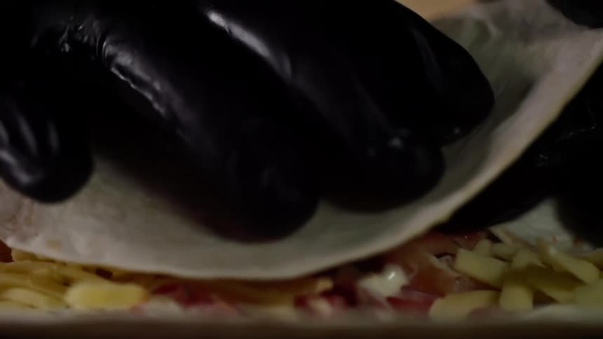 Chef wearing black latex gloves wraps a flour tortilla
