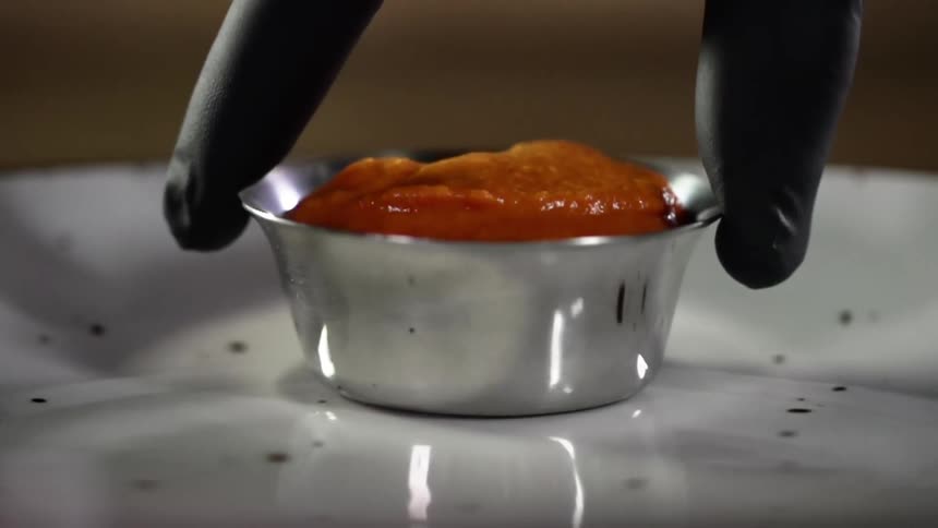 A person sets a bowl with sauce on a plate