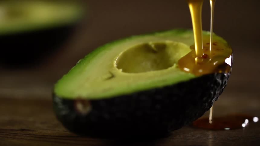 A honey type sauce pours over an avocado half