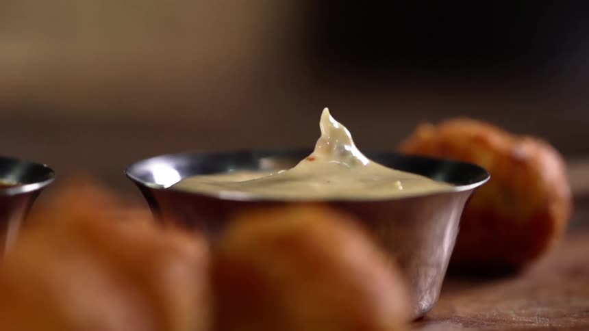 A person with gloves dipping food into sauce that is in a bowl on a table