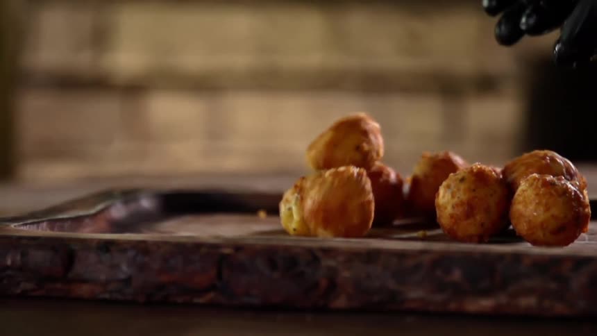 Black gloved hand puts baked donut holes on a tray