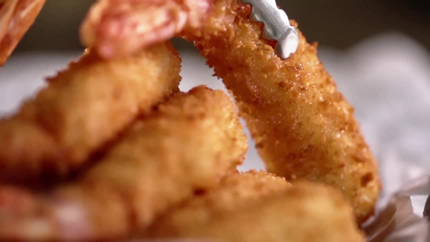 Several pieces of breaded friend shrimp are stacked on top of each other with small tongs