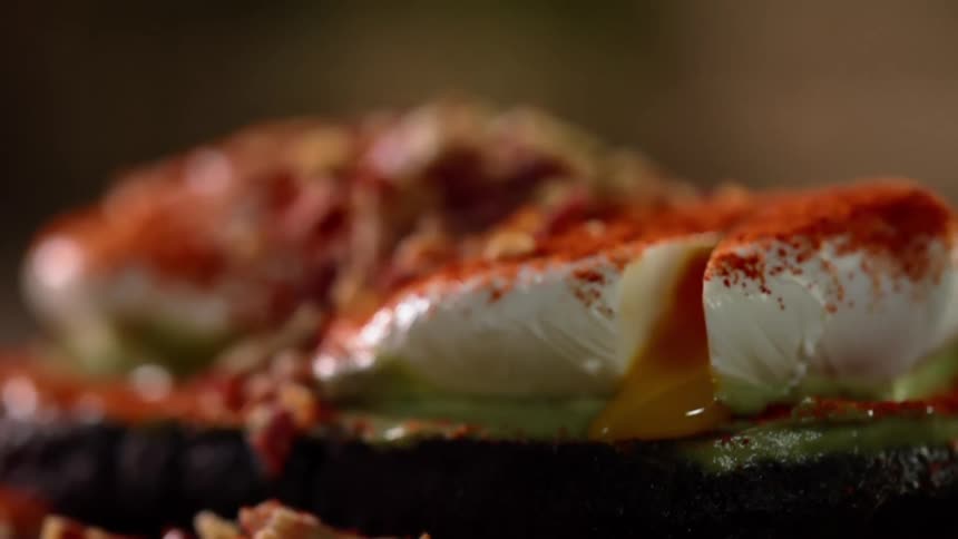 The yolk oozes out of a cut poached egg covered in paprika
