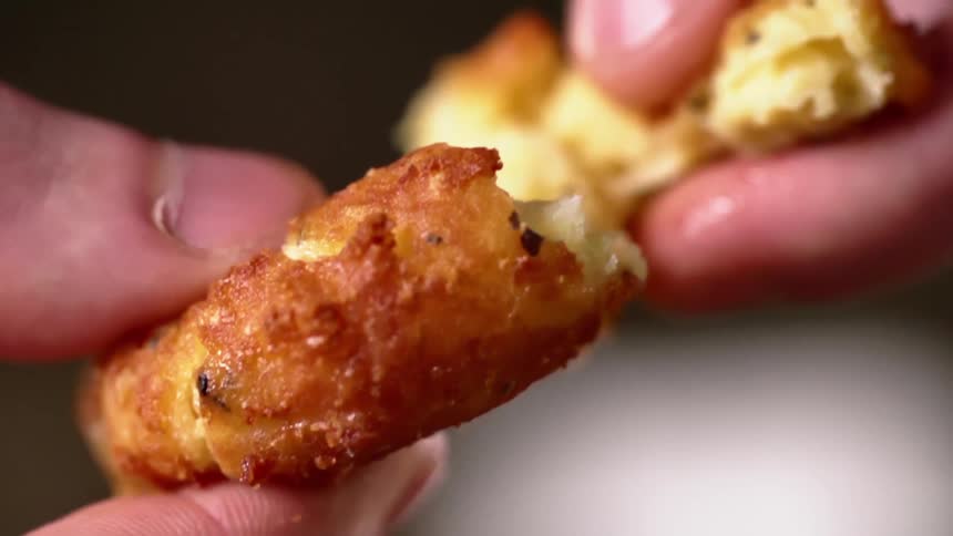 Fingers holding a golden brown fried fritter pull it apart