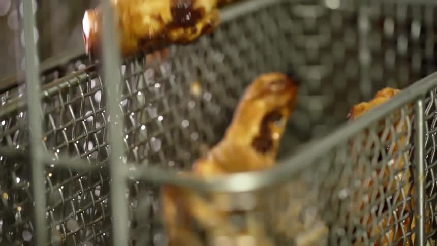 Cooked chicken pieces falling into a deep frying basket