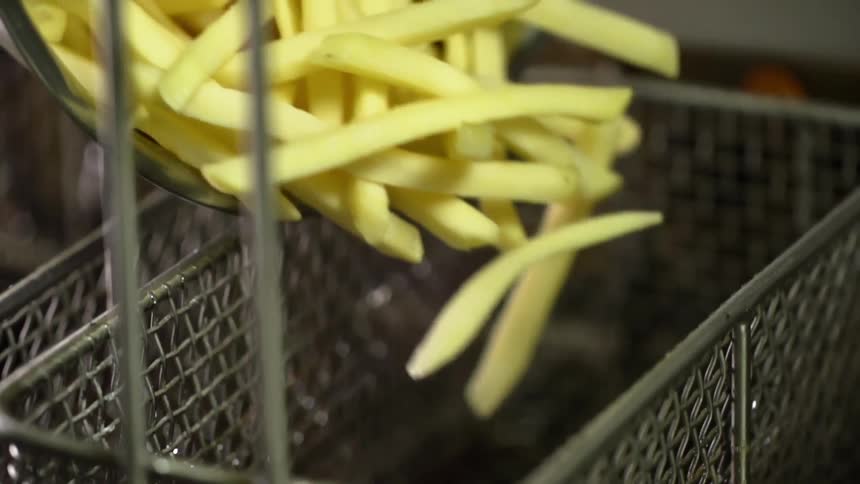 Raw french fries being poured into a deep frying basket