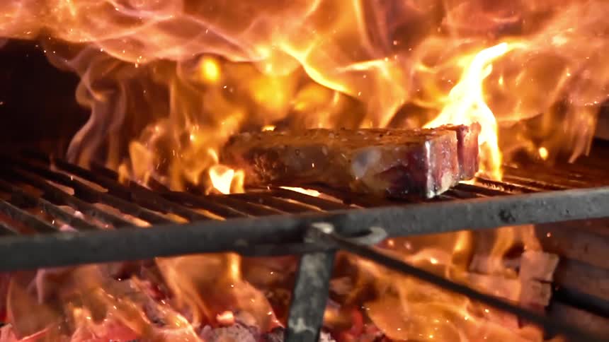 A piece of meat grilling on a grate over an open flame