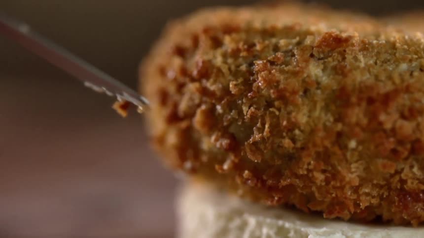 A breadcrumb covered cake is placed on the bun