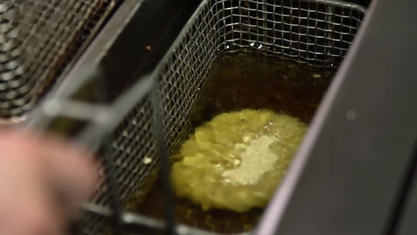 A basket containing a single battered patty is dropped into a deep fryer