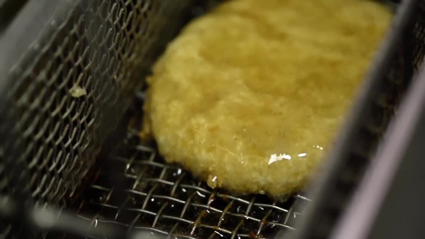 A golden brown patty in a basket is lifted out of hot bubbling oil in a fryer