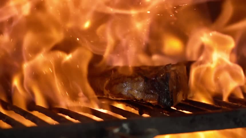 A steak cooks on a metal grill covered in flames