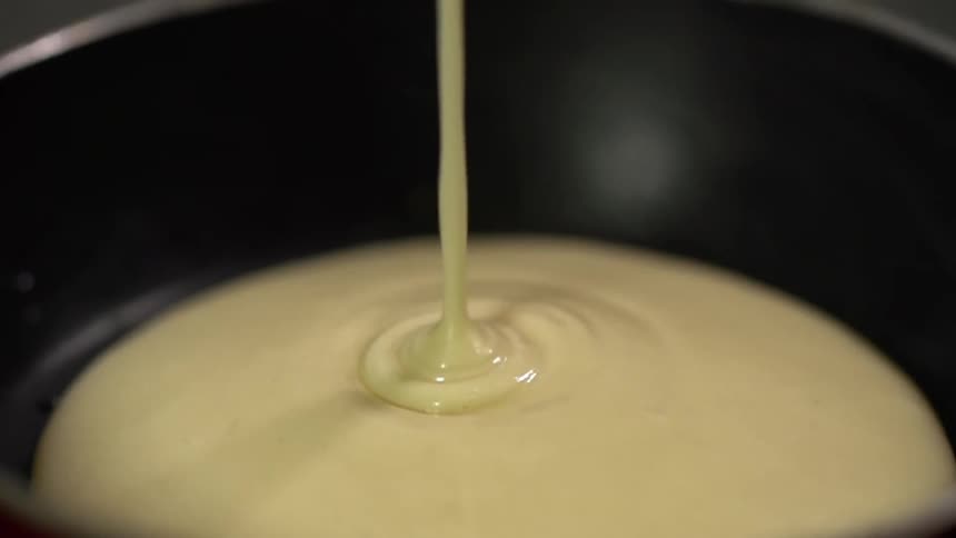Pancake batter is being poured on the hot pan