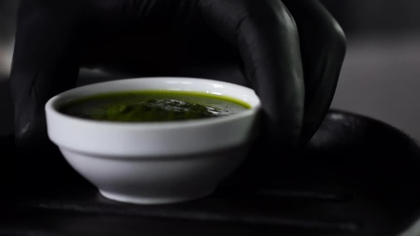A ramekin with a green dipping sauce is placed on a black plate