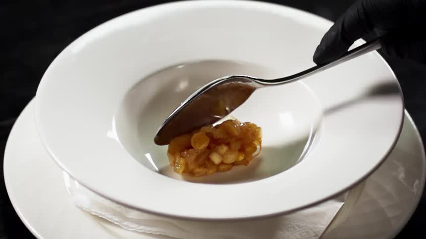 A person spoons chopped apples into a white bowl on a plate