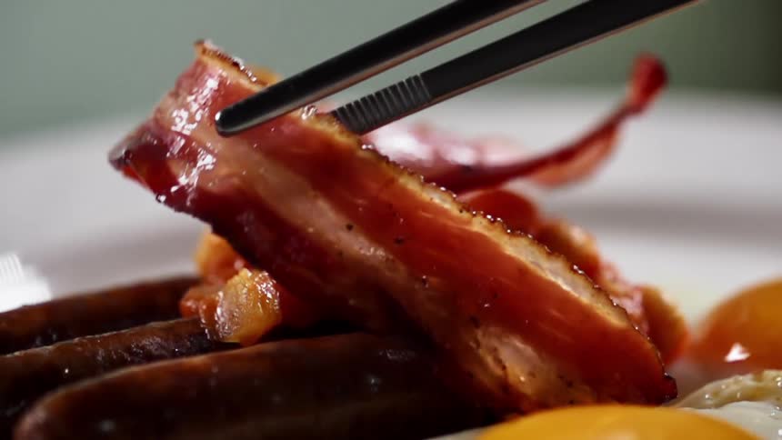 A single piece of cooked bacon is gently placed on top of three pieces of sausage