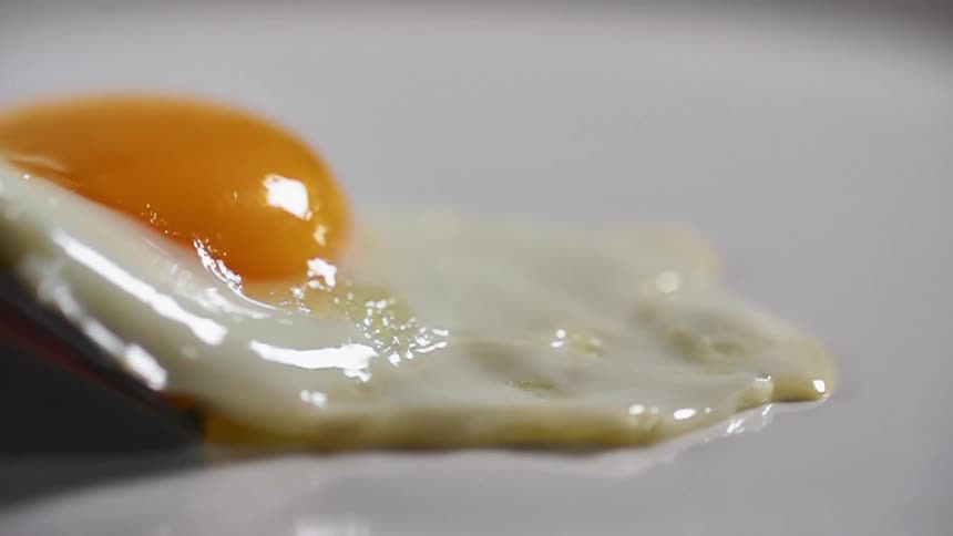 Fried egg placed on a white ceramic dish using a spatula