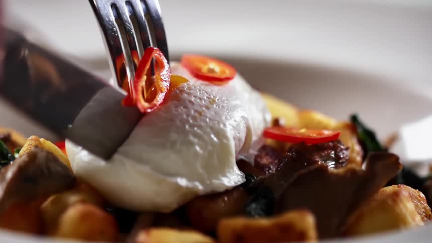 A person cuts in to an egg on a plate of food