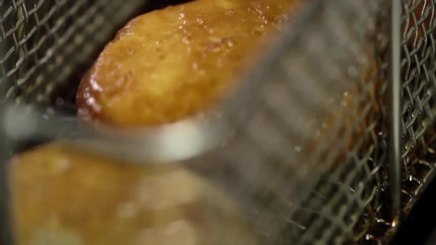 Breaded patties are lifted out of a fryer in a metal basket