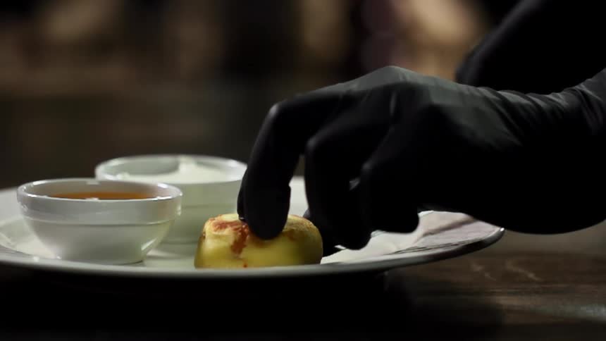 Person wearing black gloves plates food on white plate using serving utensil