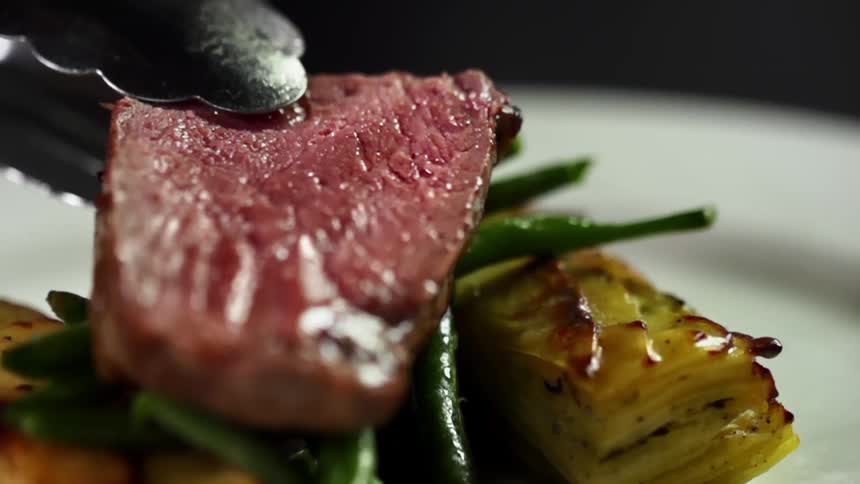 A piece of red meat is set down on a stack of green beans