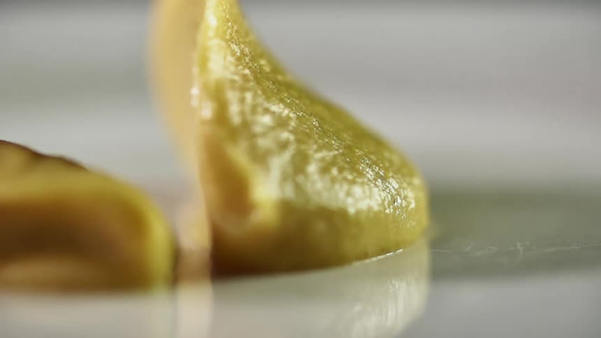 A think green sauce is slowly and carefully spooned onto a glass plate