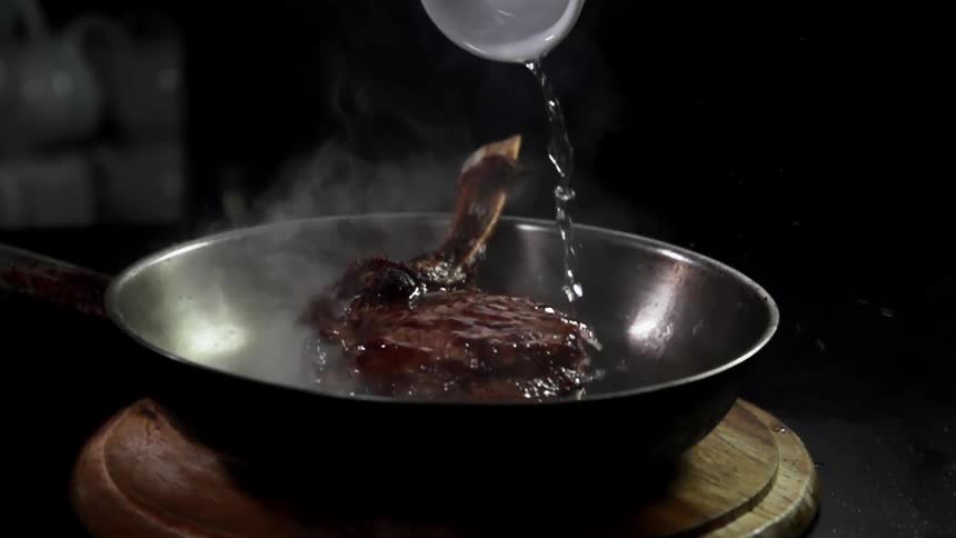 Water is poured over meat cooking in a pan