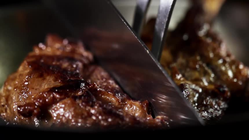A knife cuts through a cooked steak with grill marks
