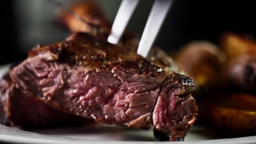 A cooking fork and knife maneuver to place a piece of steak on a plate