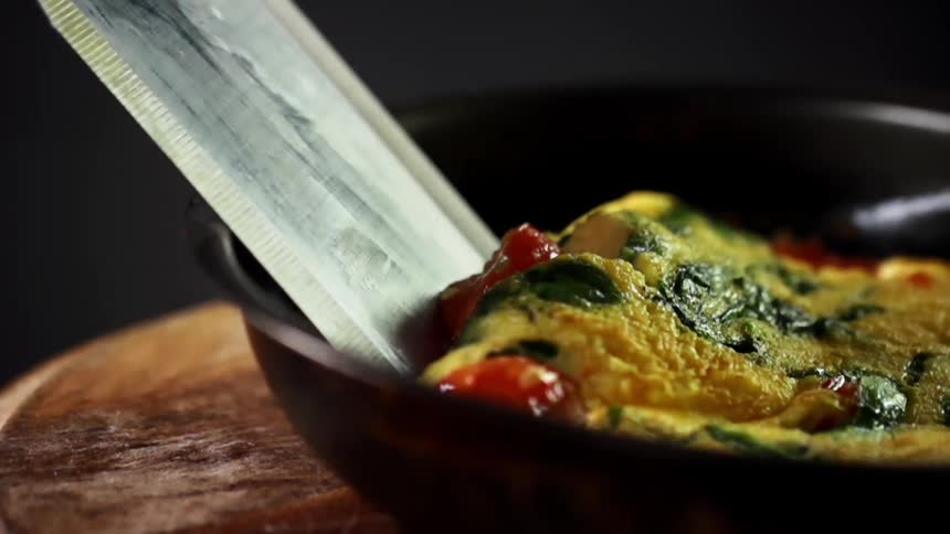 A metal utensil starts to flip over a vegetable omelette