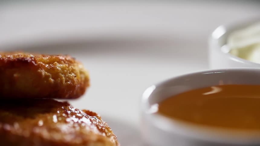 Food is placed onto a white ceramic plate next to a bowl of sauce