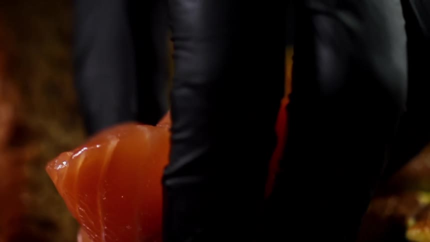 Black gloved hand places salmon on a dish