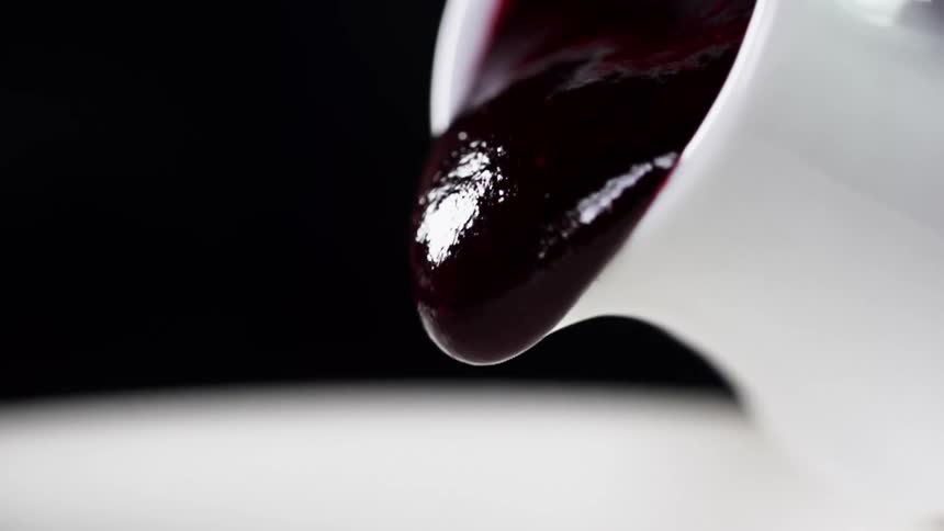 Close up of purple jam pouring out of small white pitcher