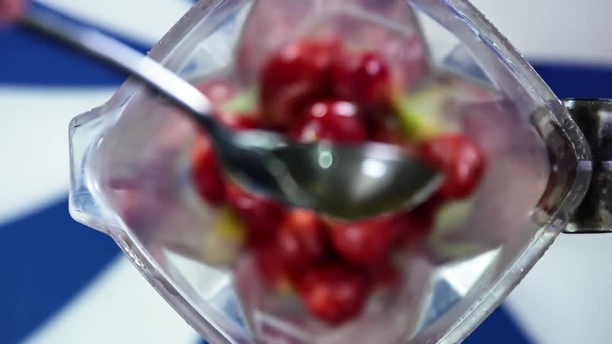 A spoonful of honey is poured over a blender full of fresh whole strawberries
