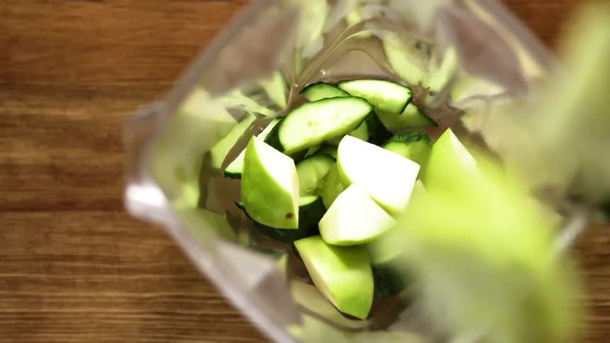 Chunks of cut cucumber and zucchini are dropped into an open blender that is not turned on yet