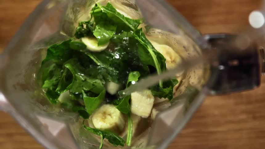 Water pours into a blender container filled with greens and banana chunks