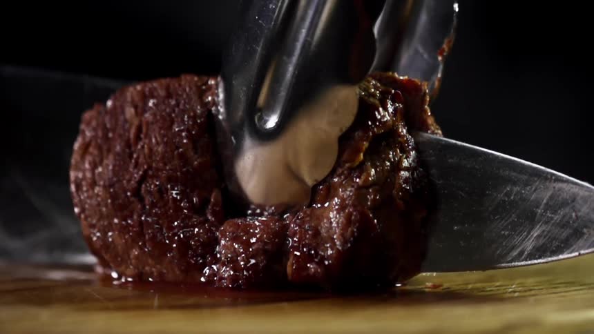 Cook with black gloves cuts juicy steak on a cutting board