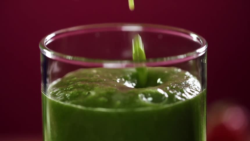 A narrow shot glass is filled with a thick blended green smoothie