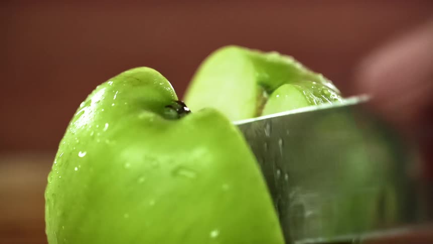 A green apple is being cut by a sharp knife