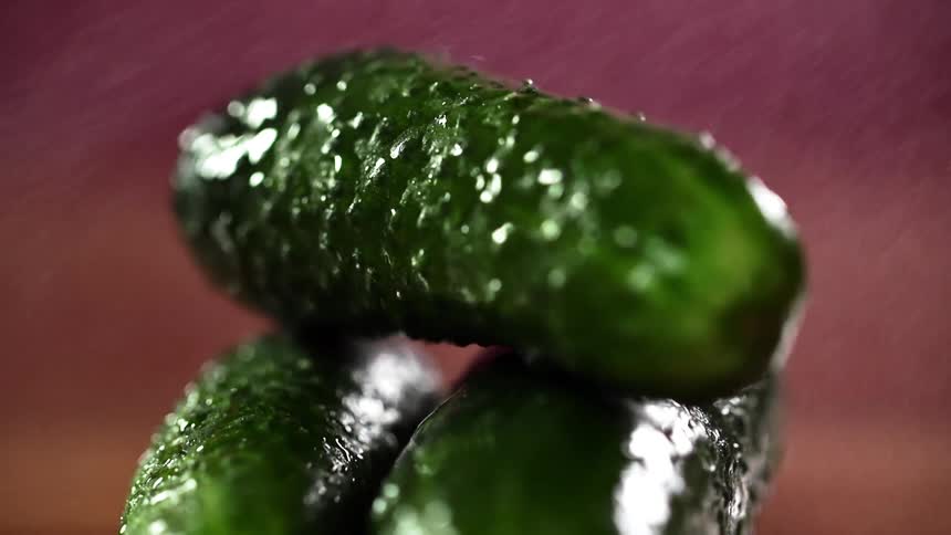 Three green pickles sprayed with water