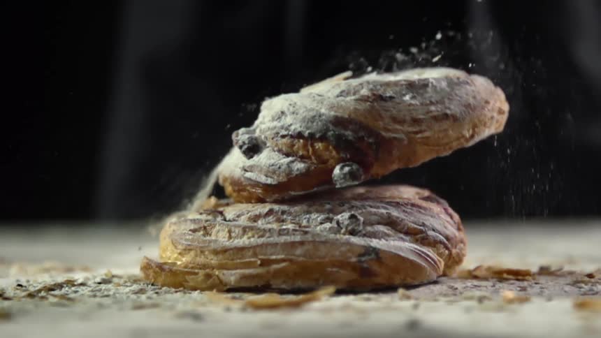 Crumbs and powdered sugar fly as a blueberry scone is dropped onto a table