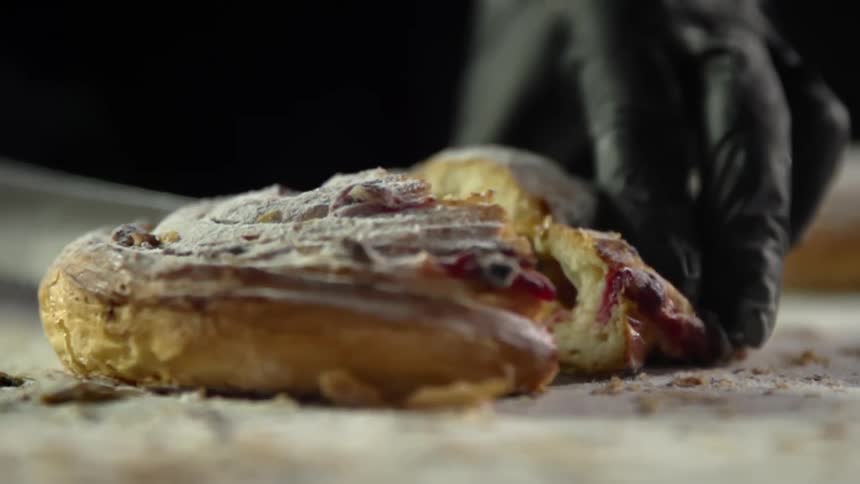 A person wearing a black glove slices a bread pastry open with a knife