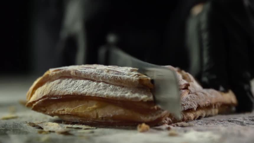A loaf of bread is gently sliced into pieces by someone using a large bread knife