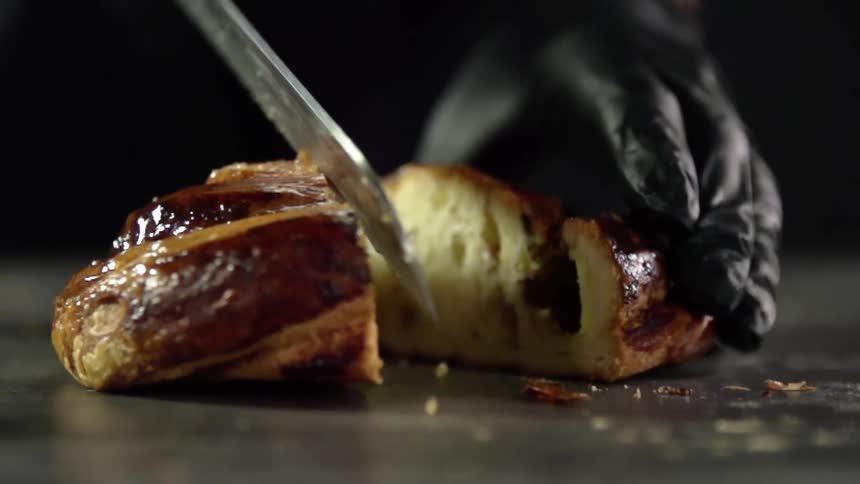 A person with gloves cutting a bread on the table with a knife