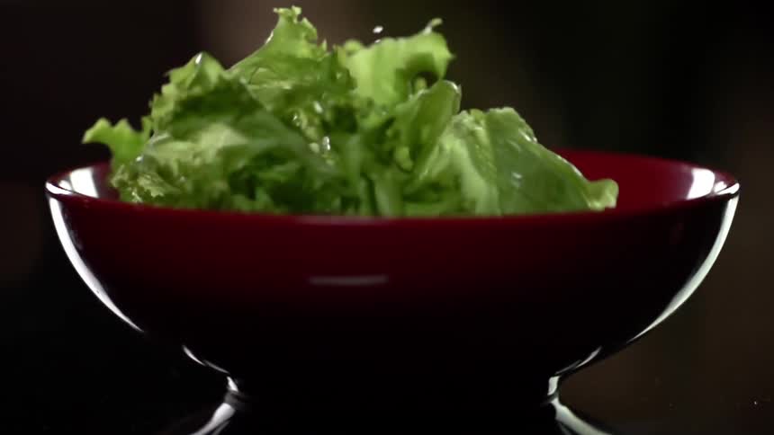 Lettuce falling in to a bowl with food in it